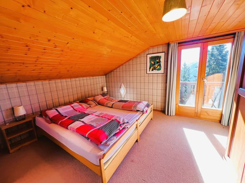 bedroom with two single beds, wooden ceiling, large window with balcony, carpet floor