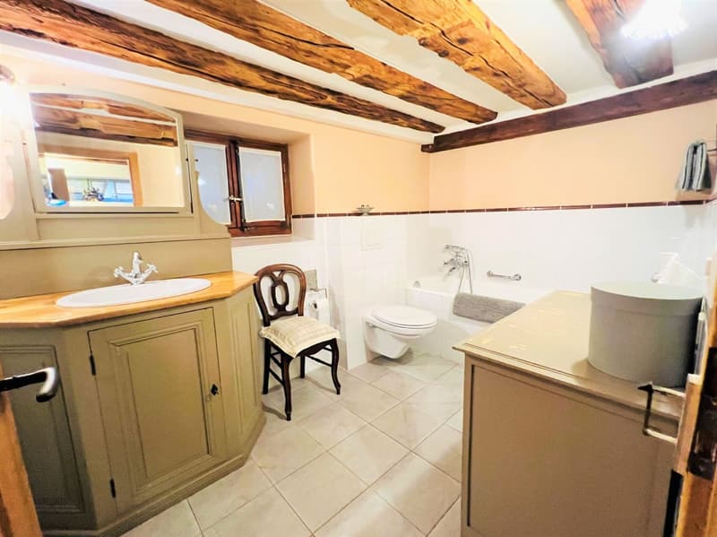 Bathroom with wooden beams, white tiles, sink, mirror, toilet, bathtub, wooden chair, wooden cabinet, towel rack