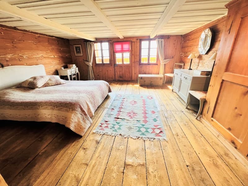 bedroom with wooden walls, wooden floor, bed, rug, desk, chair, lamp, picture frame, windows with curtains
