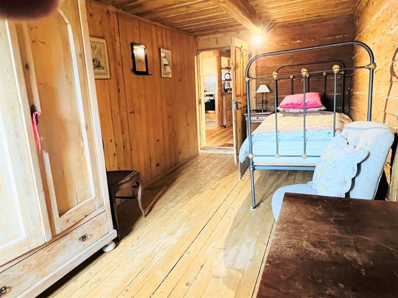 wooden walls, wooden floor, bed with blue sheets, wooden cabinet, wooden stool, lamp, nightstand, chair, picture frames