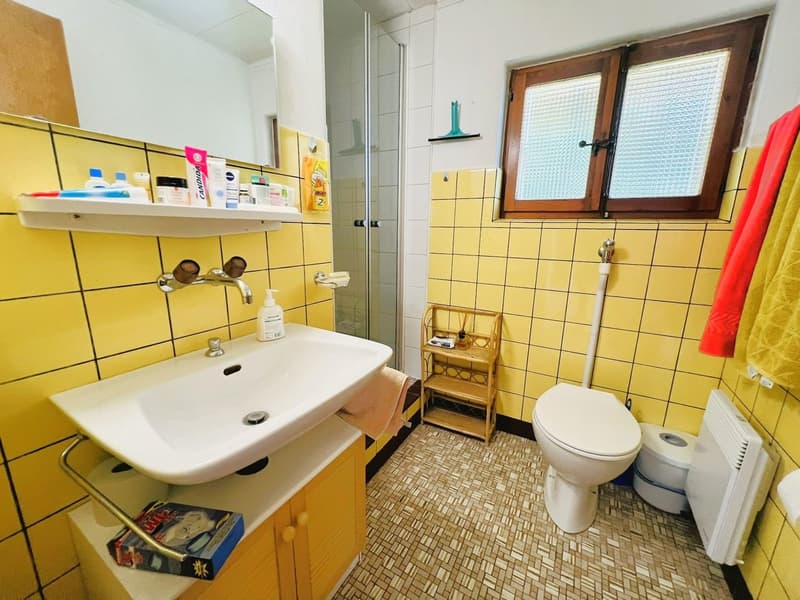 yellow tiles, white sink, white toilet, small window, shower, towel rack, radiator, toilet paper
