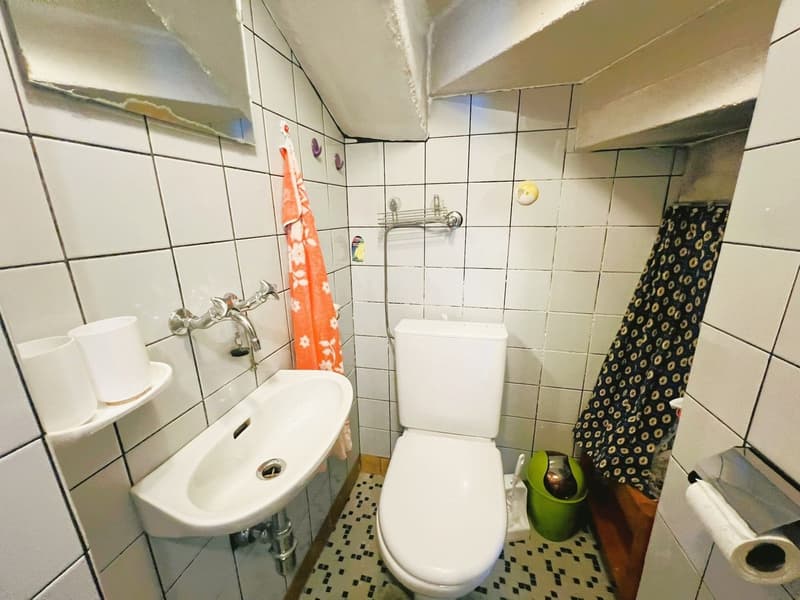 small bathroom with white tiles, white toilet, white sink, shower curtain, towel, mirror