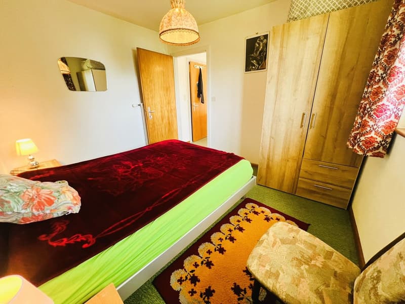 Bedroom with bed, rug, lamp, mirror, wooden wardrobe, and chair