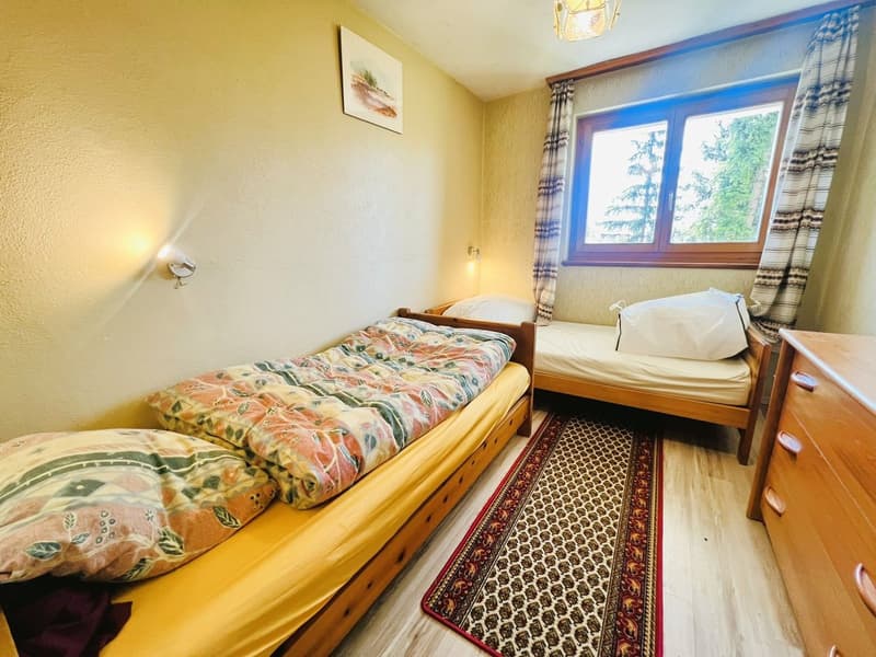 Two single beds, wooden floor, rug, wooden dresser, wall art, window with curtains