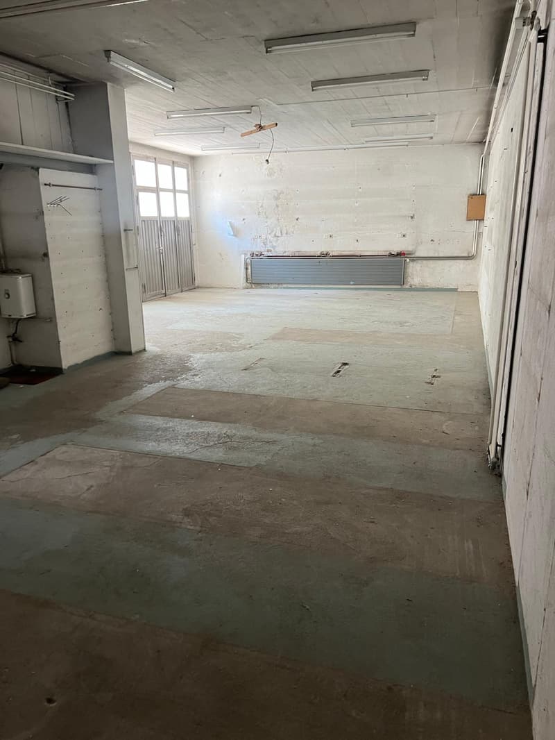 Large open space with concrete floors, exposed ceiling beams, and a ventilation system. The space appears to be a commercial or industrial property, possibly a warehouse or workshop, that is currently unfinished or under renovation.
