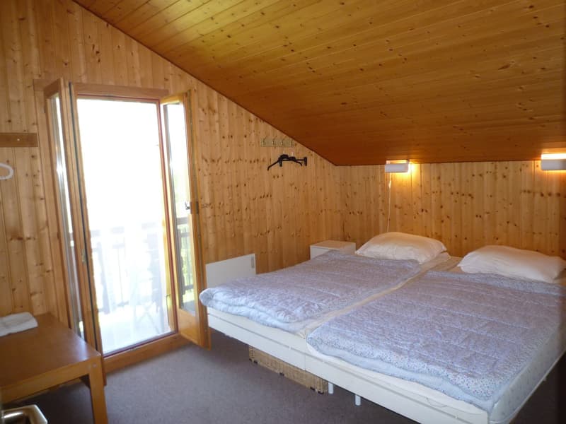 Wooden interior with slanted ceiling, two twin beds, sliding glass door leading to a balcony or terrace