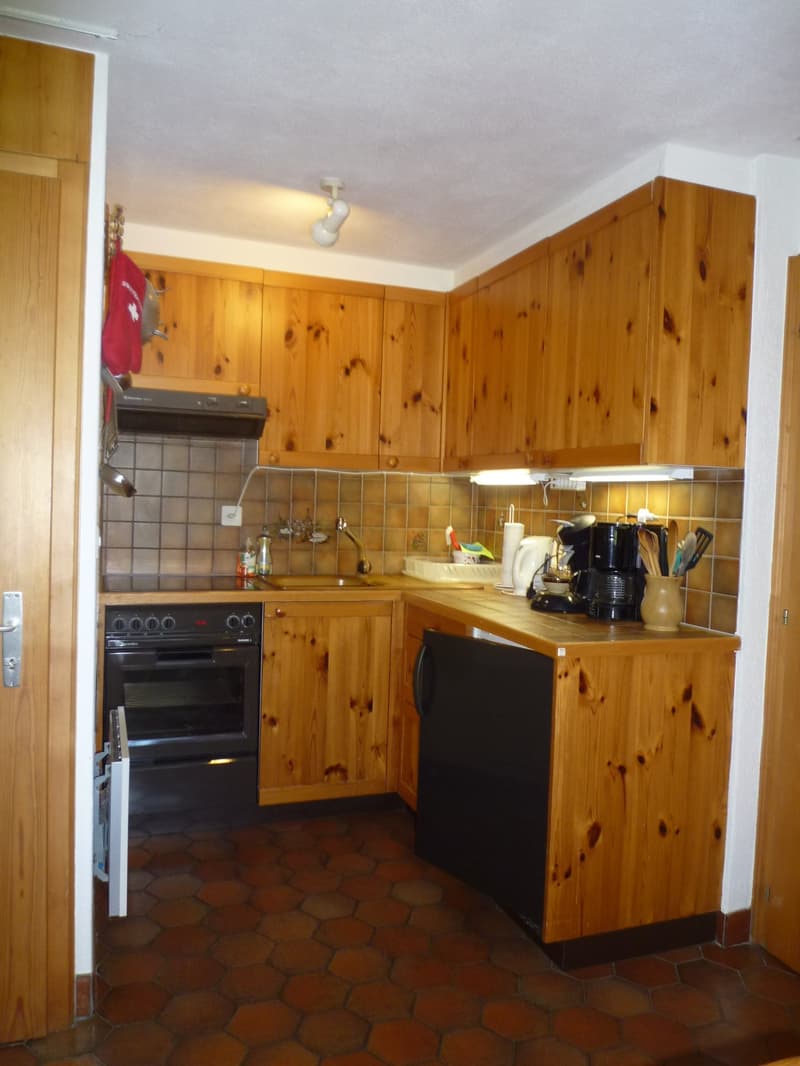 Rustic kitchen with wooden cabinets, tile flooring, stove, oven, and small appliances such as a coffee maker and blender