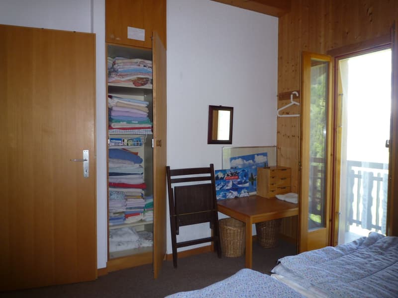 Wooden walls, built-in closet with linens, desk with chair, wicker basket, artwork on the wall, and a window with a view