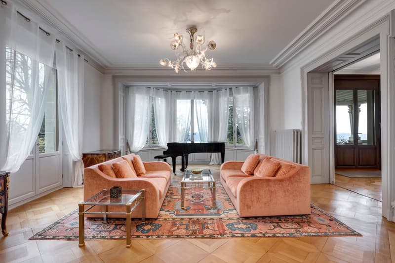 pink velvet couches, black grand piano, coffee table, area rug, large windows, chandelier