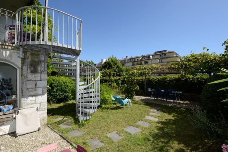 a well-maintained garden with a spiral staircase, outdoor seating area, tables, chairs, plants, and trees