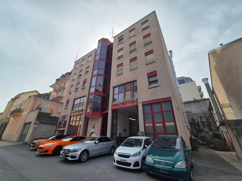 Large residential or commercial building with many windows, multiple levels, entrance with parking.