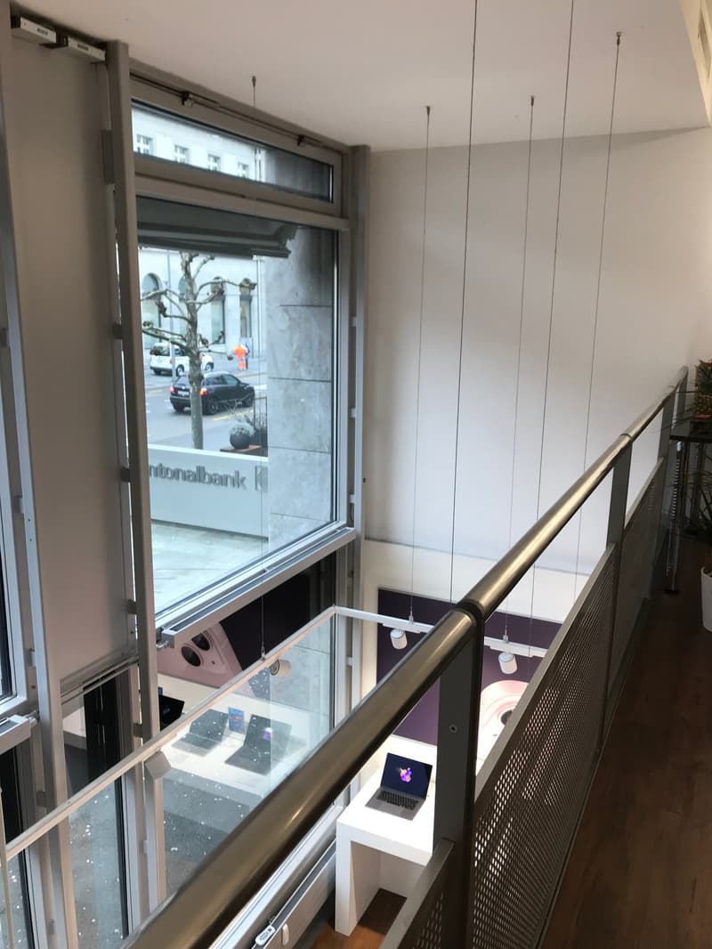 a large glass window with a view outside, glass door, railing, table with a laptop