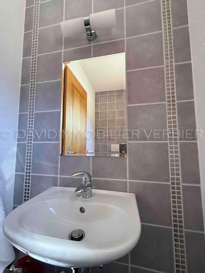 Bathroom with white sink, faucet, gray tiles, mirror, towel, wooden door, white towel, water heater