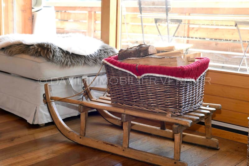 wooden sleigh filled with firewood in front of large windows