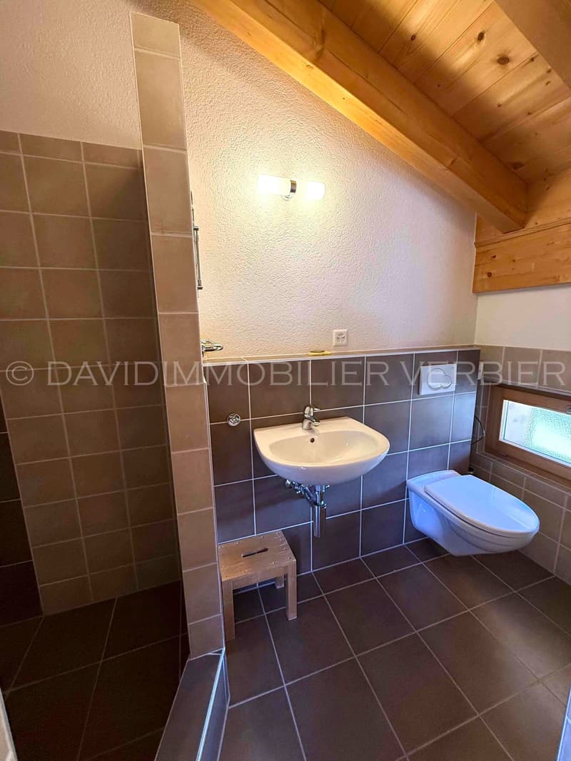 White tiled floor, white sink, toilet, shower stall, wooden ceiling, wall outlet