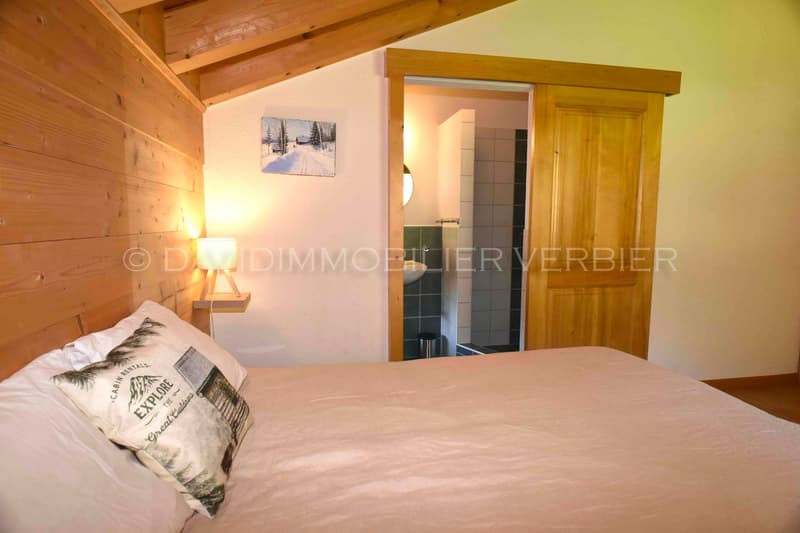 wooden ceiling, bed, pillows, small nightstand, lamp, open door leading to the bathroom, tiles, mirror
