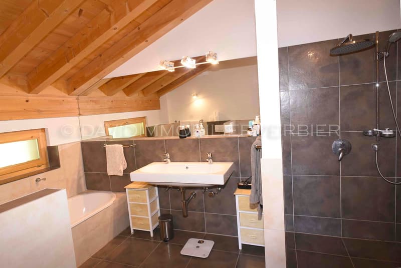 Bathtub, white sink, tiled floors, tiled walls, shower, two faucets, wooden ceiling