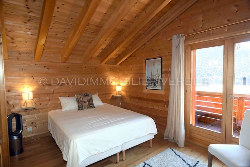 a cozy wooden room with bed, wooden beams ceiling, lamp, a carpet, double doors leading to balcony