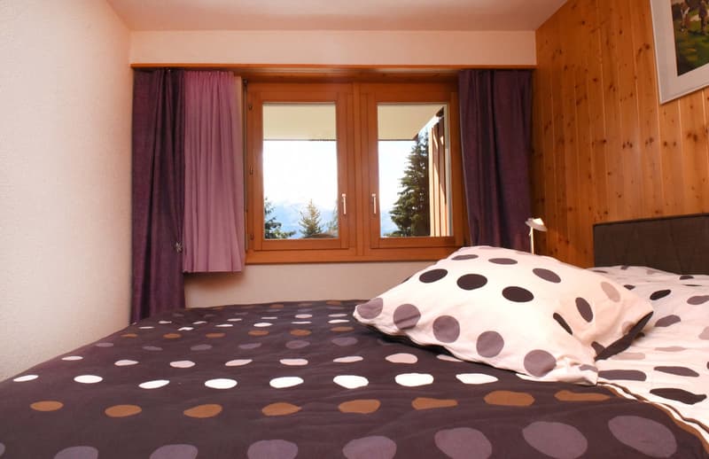 bedroom with bed, polka dot bedspread and pillows, window with view of mountains