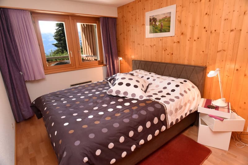 bedroom with double bed, hardwood floors, wall-mounted picture frame, nightstand with lamp, curtains