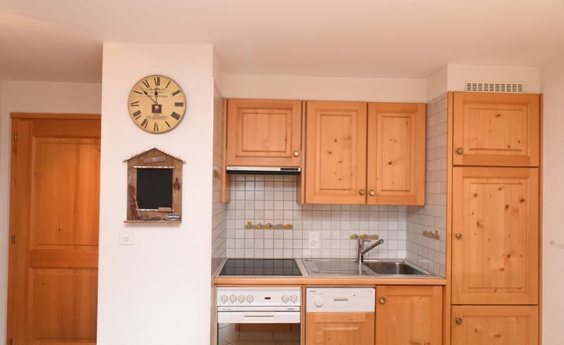 wooden cabinets, white tiled walls, black stovetop, white dishwasher, wooden clock, wooden door