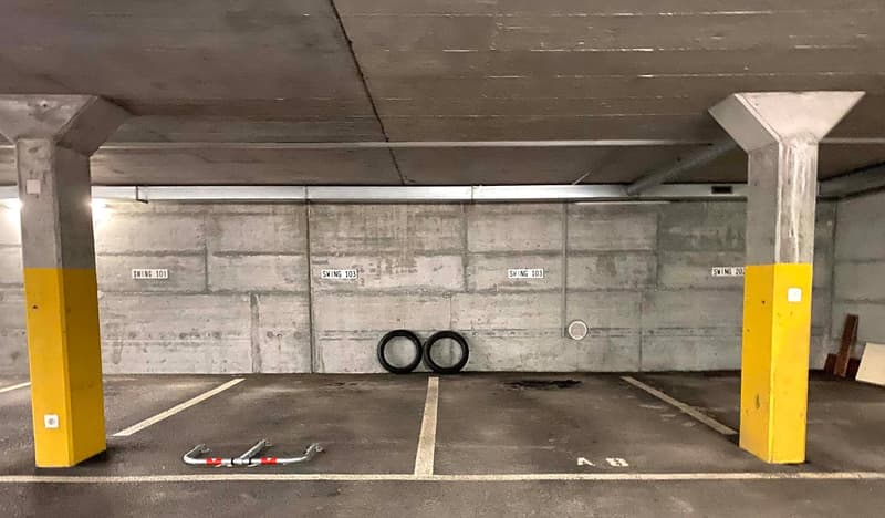 Empty parking space, concrete floor, two yellow pillars, parking tags, empty wall, a bike lock