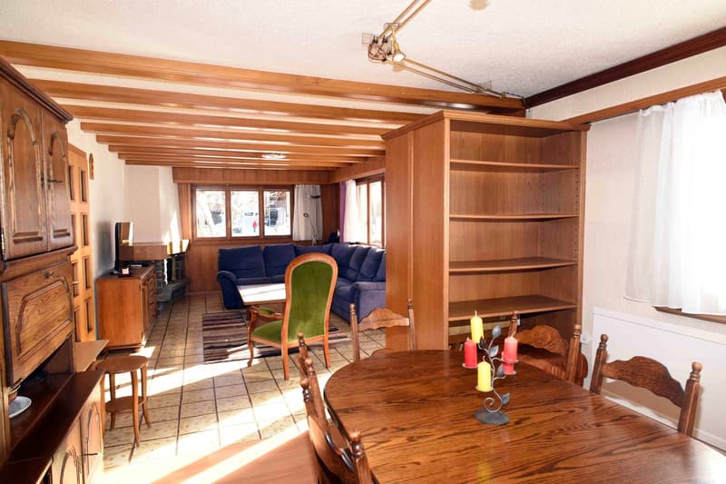 wooden dining table, green and brown chairs, wooden shelves, wooden cupboard, blue sofa, carpet, wooden table, candle stand, windows