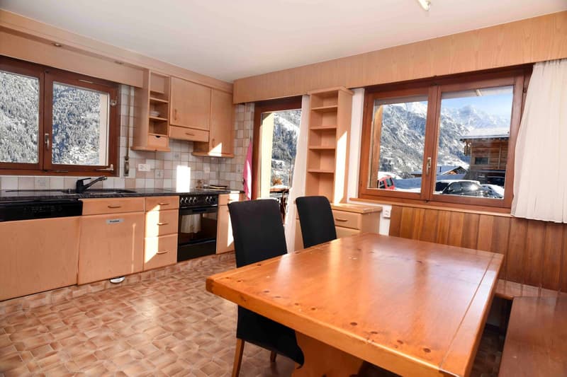 Kitchen area with tiled floor, wooden cabinets, kitchen counter, wooden dining table, oven, sink, dishwasher, two black chairs, large windows with mountain view
