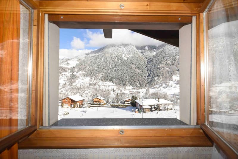 View of snowy mountains and surrounding wooden chalets from a wooden framed window