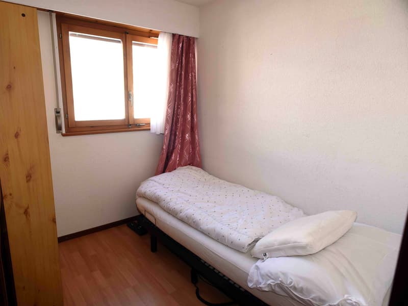 Small room with bed, wooden floor, white walls, window with curtains