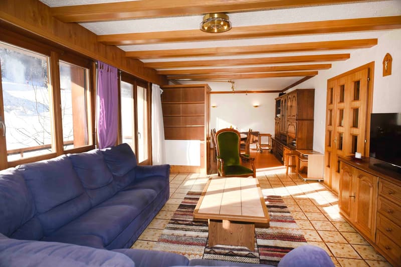 modern living room with blue couch, wooden coffee table, green chair, TV, wooden cabinets, windows with curtains