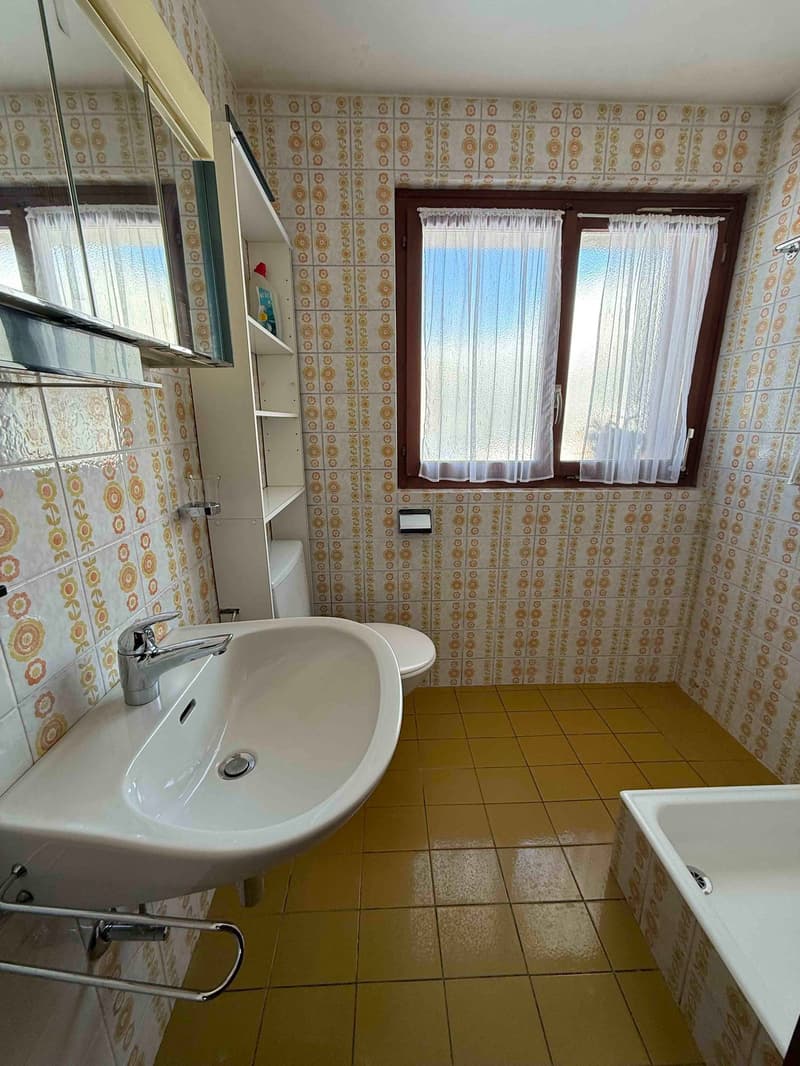Bathroom: white sink, white bathtub, white toilet, window with curtains, tiled floor, shelves, mirror, silver faucet
