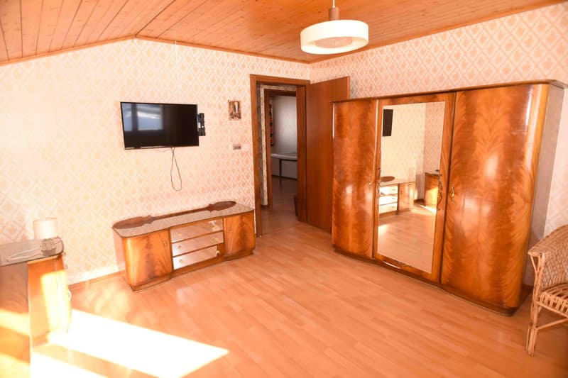 Living room: mounted TV, lamp, large wooden cabinet with drawers, wooden door, wooden wardrobe with mirror, wooden chair