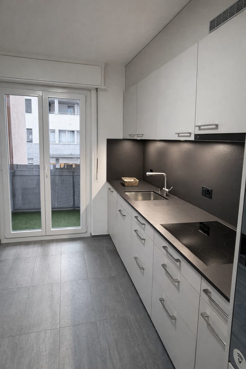 Modern kitchen with a glass door, countertop, sink, faucet, white cabinets, gas stove, tiled floor.