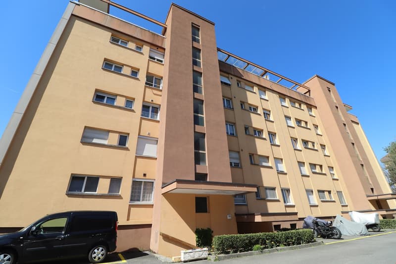 6 story building, beige colored wall, many windows, parking place in front of the building