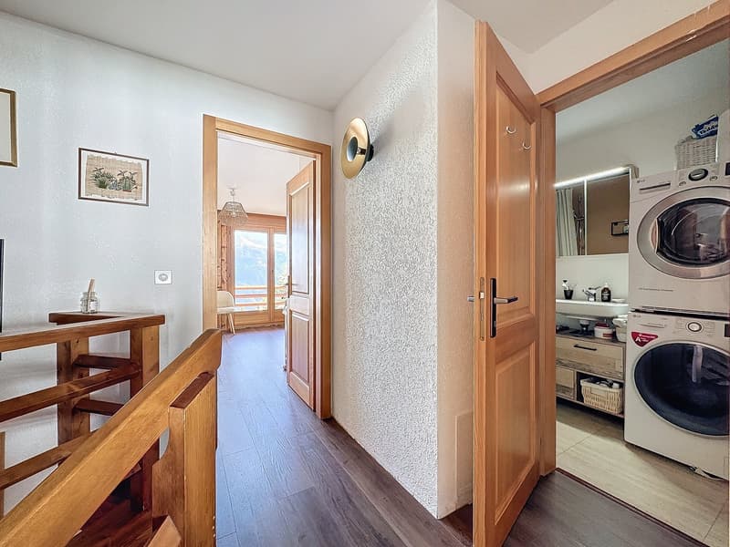 white walls, wooden floor, open door to the laundry room with washing machine and dryer, wooden handrail, picture frame