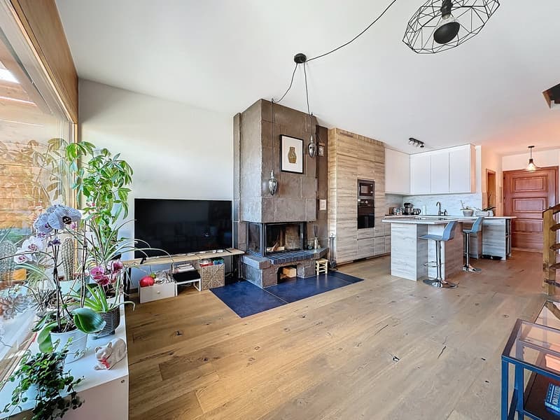 Living room with wooden floor, a fireplace, a large screen TV, plants, and kitchen bar stools