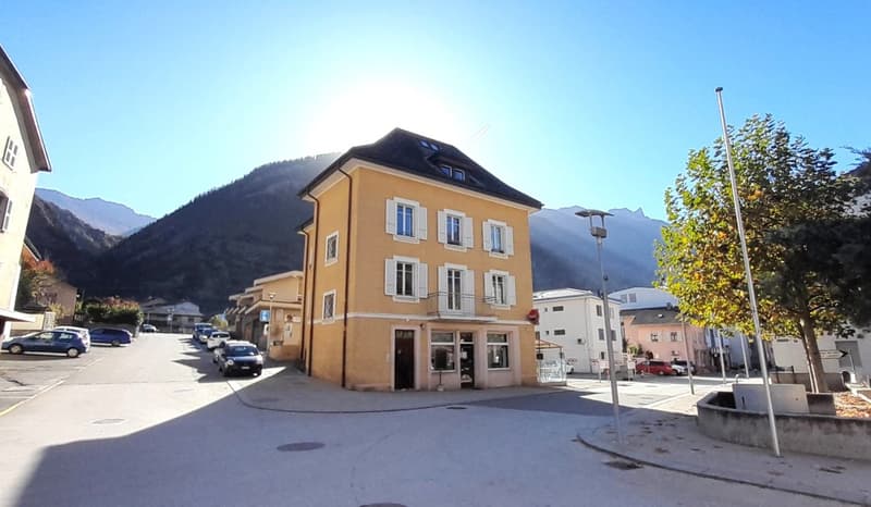 two-story building, multiple cars parked, street lamps, mountains in the background