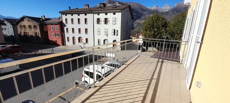 Balcony, white metal railing, tile floor, cars parked on street, building, mountain in background
