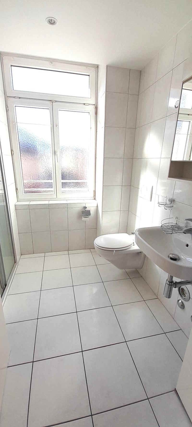 white tiled floor, white walls, white toilet, white sink with faucet, mirror, window with view
