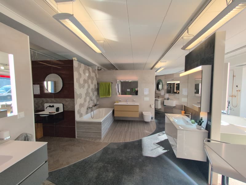 modern bathroom with white bathtub, wall-mounted sink, mirror, tiled walls, ceiling lights, and a green towel hanging on the wall.
