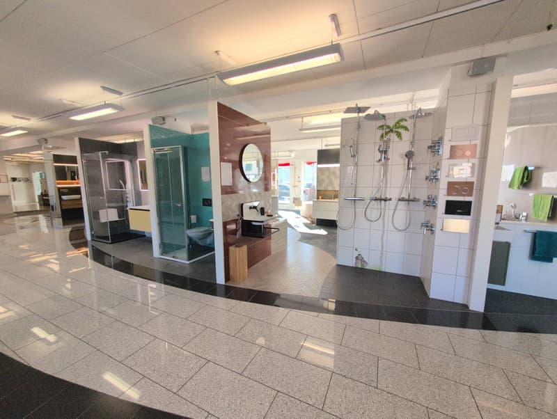 Showroom with tiled floors, a modern and clean bathroom display, large glass doors, various lighting fixtures on the ceiling, a toilet and a sink in the bathroom display