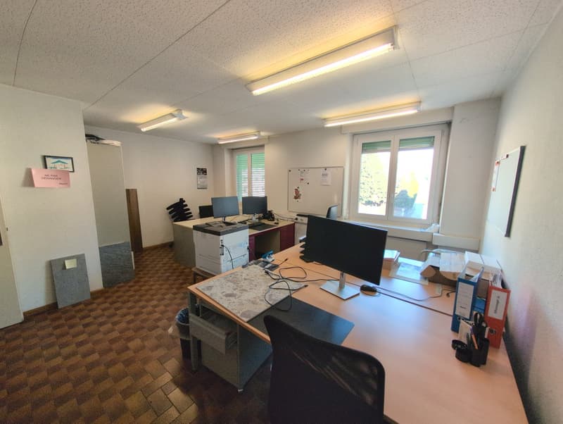 Desks with computers, printer, office supplies, framed picture, window with blinds, light fixtures, trash bin