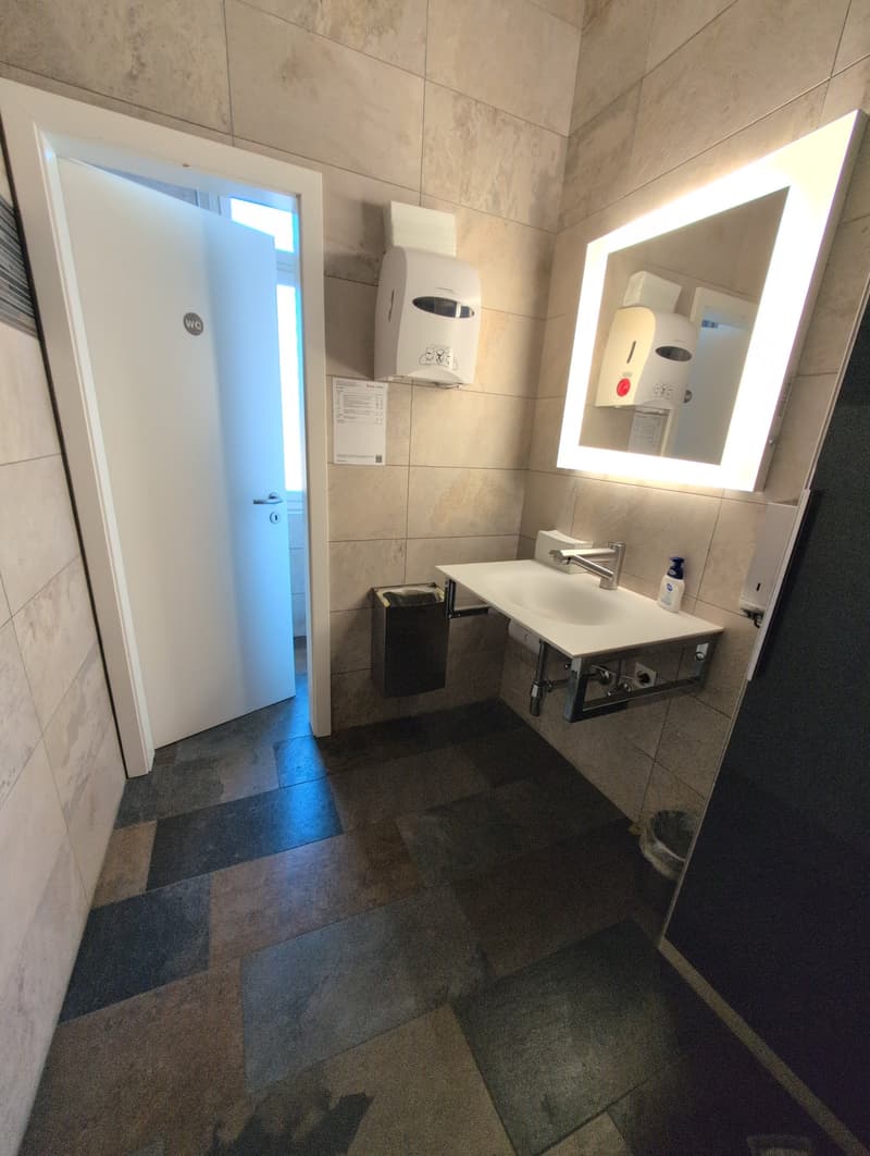 white sink with silver faucet, mirror, hand soap, tissue holder, trash can, tiled flooring