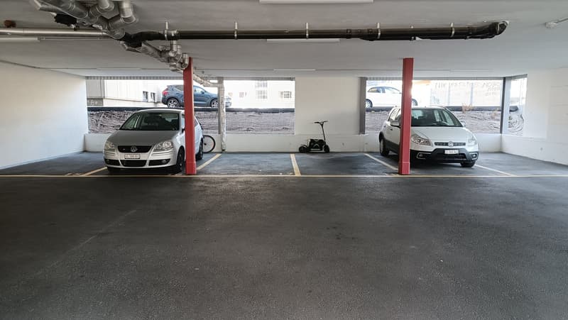 undercover parking lot with two vehicles parked in designated parking spaces and a scooter