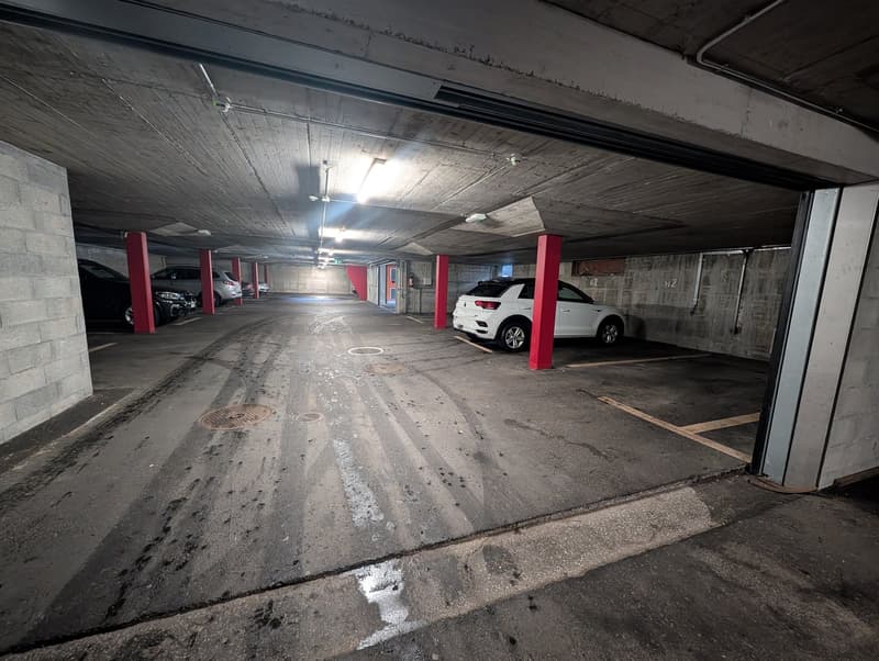 underground parking lot, red pillars, well lit, few cars parked