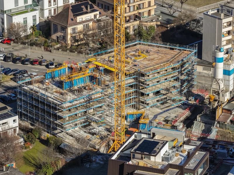 Aerial view of an ongoing construction site with multiple floors and several parked cars in front of the site.