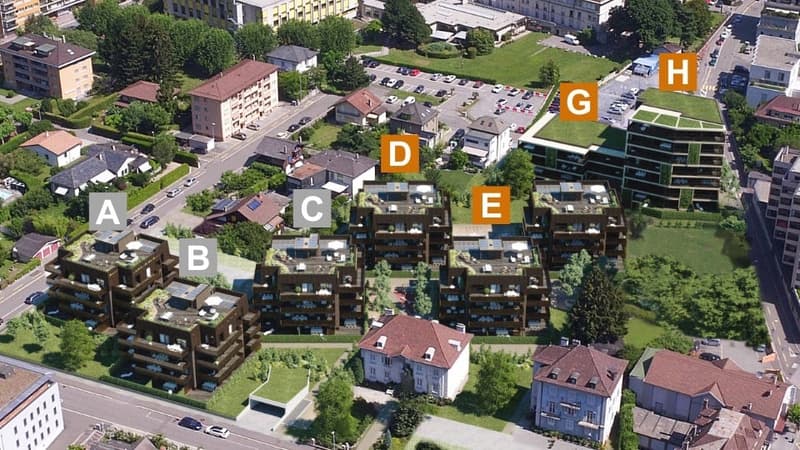 Aerial view of apartment complex, includes buildings labeled A to E and H, various sized green spaces, roads and parking spaces
