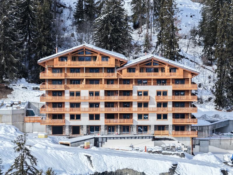 multi-story building, wooden balconies, snow-covered roof, surrounded by pine trees, snowy landscape