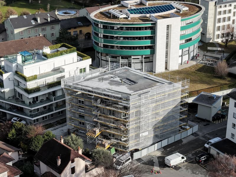 Aerial view of a building complex under construction with multiple stories, green roofs, and scaffolding.